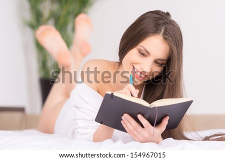 Making notes. Cheerful young woman writing something in her note pad while lying on the sofa