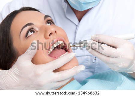 Patient at dentist office. Close-up of beautiful young woman sitting at the chair in dental office and doctor examining teeth