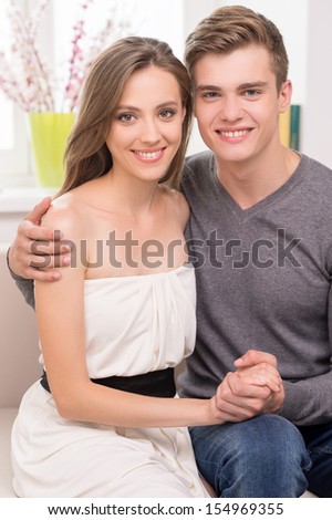 Loving couple at home. Beautiful young couple hugging and smiling while sitting on the couch