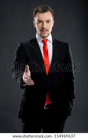 Businessman. Confident young men stretching out his hand for shaking while standing isolated on black