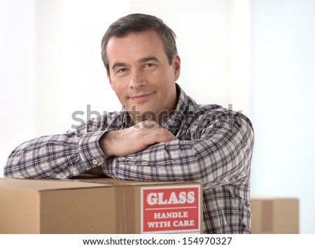 House moving. Cheerful middle-aged man leaning at the cardboard box and smiling