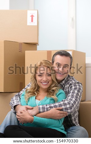 House moving. Beautiful middle-aged couple sitting together near the cardboard boxes and smiling