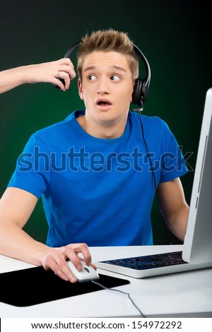 Gamer. Shocked teenage boy playing video games at his computer while someone taking off his headphone