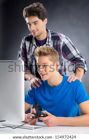 Gamers. Cheerful young gamer playing video games at the computer while his friend watching at monitor