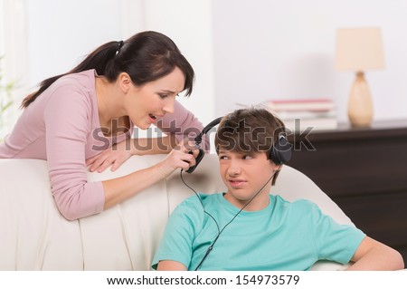 Mother and problem child. Angry mother trying to talk with her son listening music in headphones