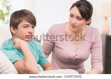 Mother and problem child. Frustrated mother trying to talk with her depressed son sitting on the couch