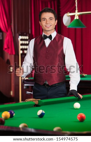 Pool player. Cheerful young pool player holding cue and looking at camera