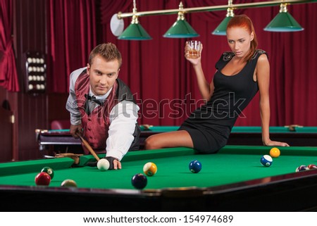 Playing pool. Beautiful young woman standing near confident young man playing pool