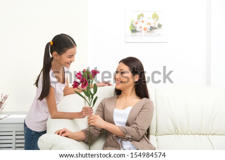 Mother and daughter. Cheerful daughter presenting flowers to mother