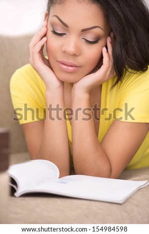 Woman reading. Beautiful African descent women reading a book while lying on the couch at home