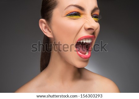 Woman screaming. Furious young women with beautiful make-up shouting and looking away while isolated on grey
