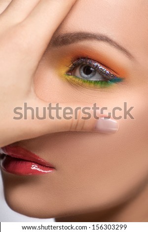 Beautiful make-up. Young women with beautiful make-up looking away and covering face with hand while isolated on grey