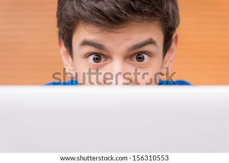 Teenager at the computer. Surprised teenage boy looking out of the laptop
