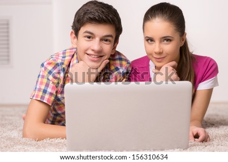 Leisure time. Two cheerful teenagers using computer together and smiling