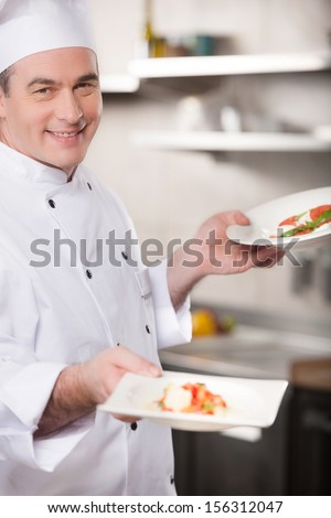 Confident chef. Cheerful chef holding plates with food and smiling