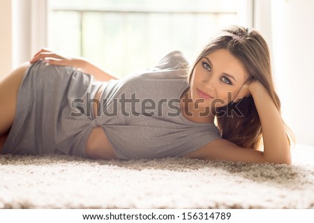 Day off at home. Attractive young woman in dress lying on the carpet and smiling