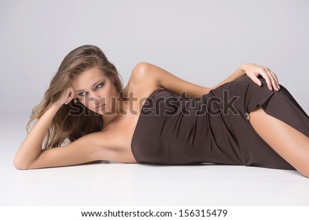 Gorgeous woman. Beautiful young fashion model lying on side while isolated on grey