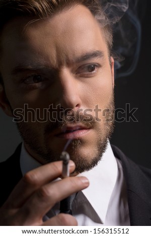 Man smoking. Bossy young man in formalwear smoking while standing isolated on black