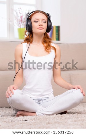 Red hair beauty. Beautiful red hair woman in headphones listening to the music while sitting in lotus position