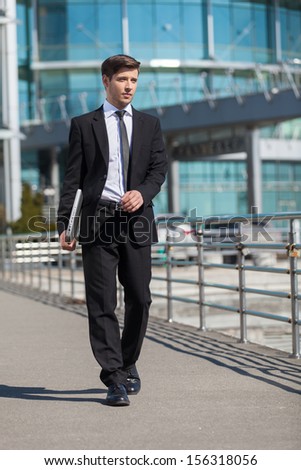 Successful businessman. Full length of cheerful young men in formalwear holding laptop while walking outdoors