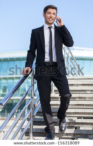 Successful businessman. Full length of cheerful young men in formalwear talking on the mobile phone while going downstairs