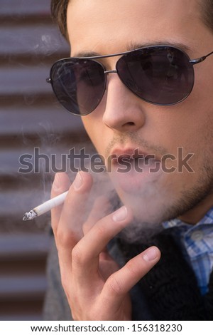 Man smoking. Thoughtful young man in sunglasses smoking