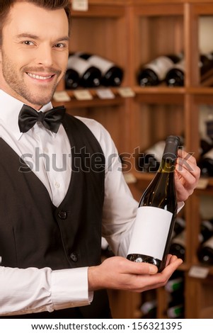 Confident sommelier. Handsome young sommelier holding a wine bottle and smiling