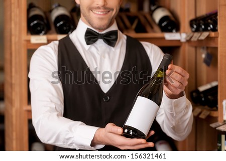 Confident sommelier. Cropped image of cheerful young sommelier holding a wine bottle and smiling