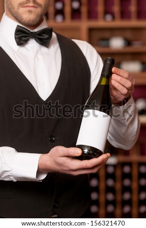 Confident sommelier. Cropped image of confident young sommelier holding a wine bottle and smiling