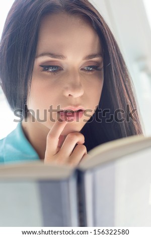 Woman reading. Beautiful young woman reading book and touching lips by finger