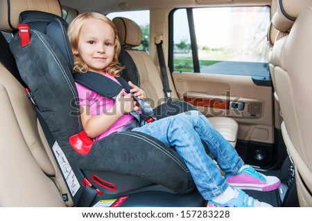 Small girl is sitting in child cat seat, looking at the camera