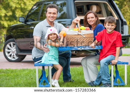 Family with two kids at picnic, sitting together at the table with fruit basket