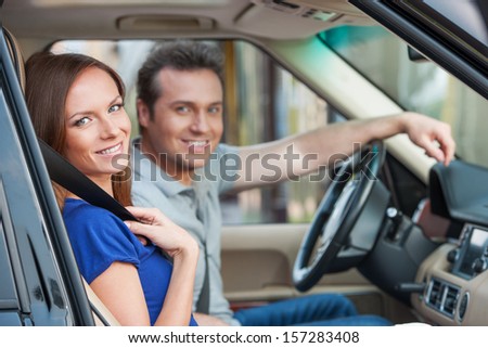 Loving couple in a car looking in camera, toothy smile