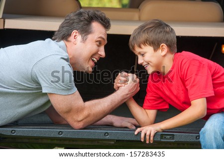 Father and son is wrestling at the pened car boot. Smiling and enjoying time together