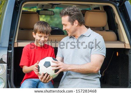 Father And Son Sit Near Car With Opened Boot And Going To Talk About Football Game