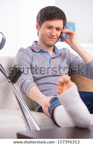 Man talking by phone with broken leg, having sad face