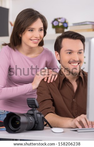 Two people are seating by computer. Indoors shoot  with big toothy smile