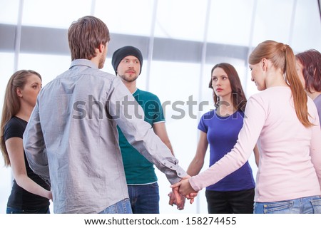 Group of people standing in circle. Holding hands, looking at each other