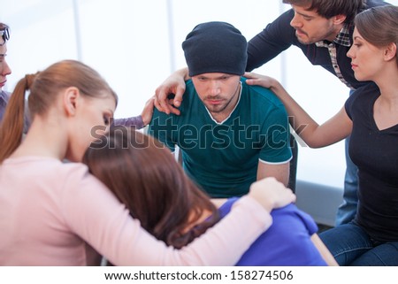 Several people comforting young man on background. Young woman comforting another woman on foreground