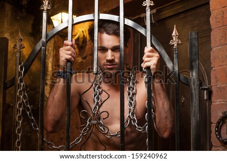 Sexy man standing behind metal gates. With metal chain on neck