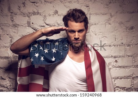 Young handsome man posing with American flag. Saluting like soldier