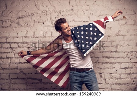 Handsome man posing with American flag. Smile and using flag like cloak