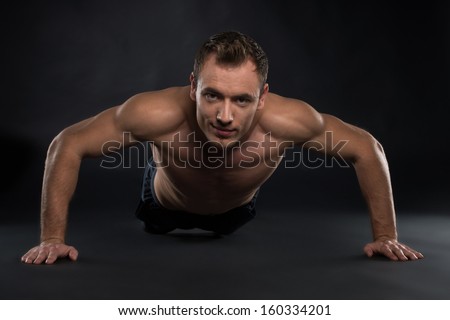 Handsome Young sport man. Fitness muscle model guy making push ups exercise over black background