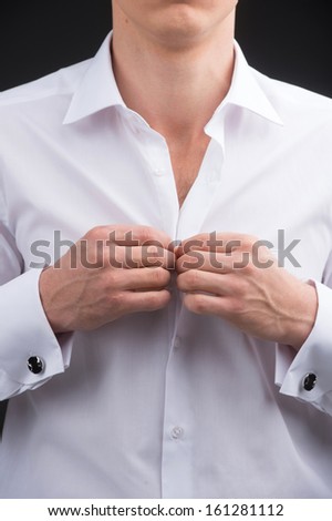 Close up of man buttoning white shirt. Cut without face