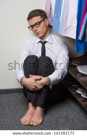 Sad man sitting near wardrobe full of clothes. Looking pisimistic