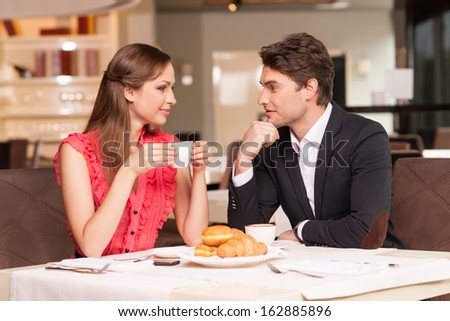 Loving couple having romantic breakfast at the restaurant. Looking at each other and smiling.