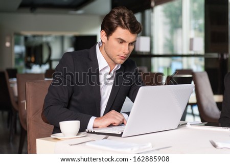 Handsome businessman working with laptop. Sitting at the restaurant and drinking coffee.
