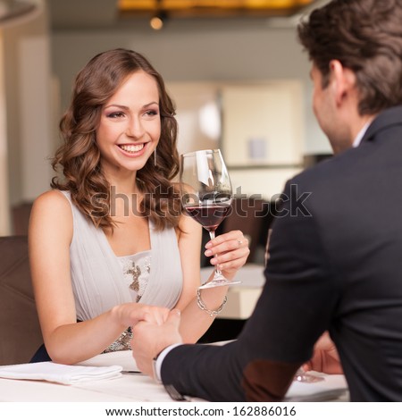 Handsome man holding his girlfriend hand. Drinking wine and smiling