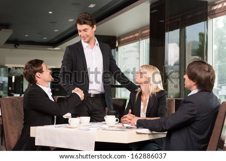 Handsome Business Man Greeting Group Of People. Sitting At Restaurant Drinking Coffee