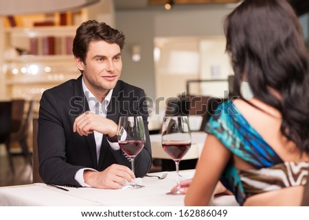 Seducing  handsome man looking at beautiful dark hair woman with wine glasses. Romantic and love mood